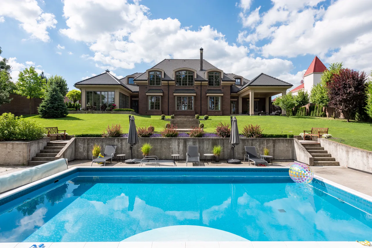 A backyard pool with a lawn and a brick house behind it